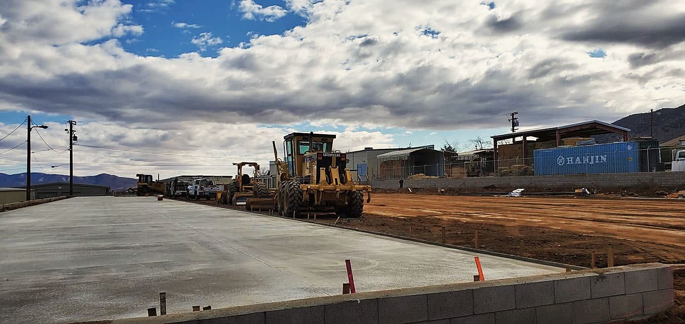Motor graders working beside a freshly poured concrete slab on a commercial pad