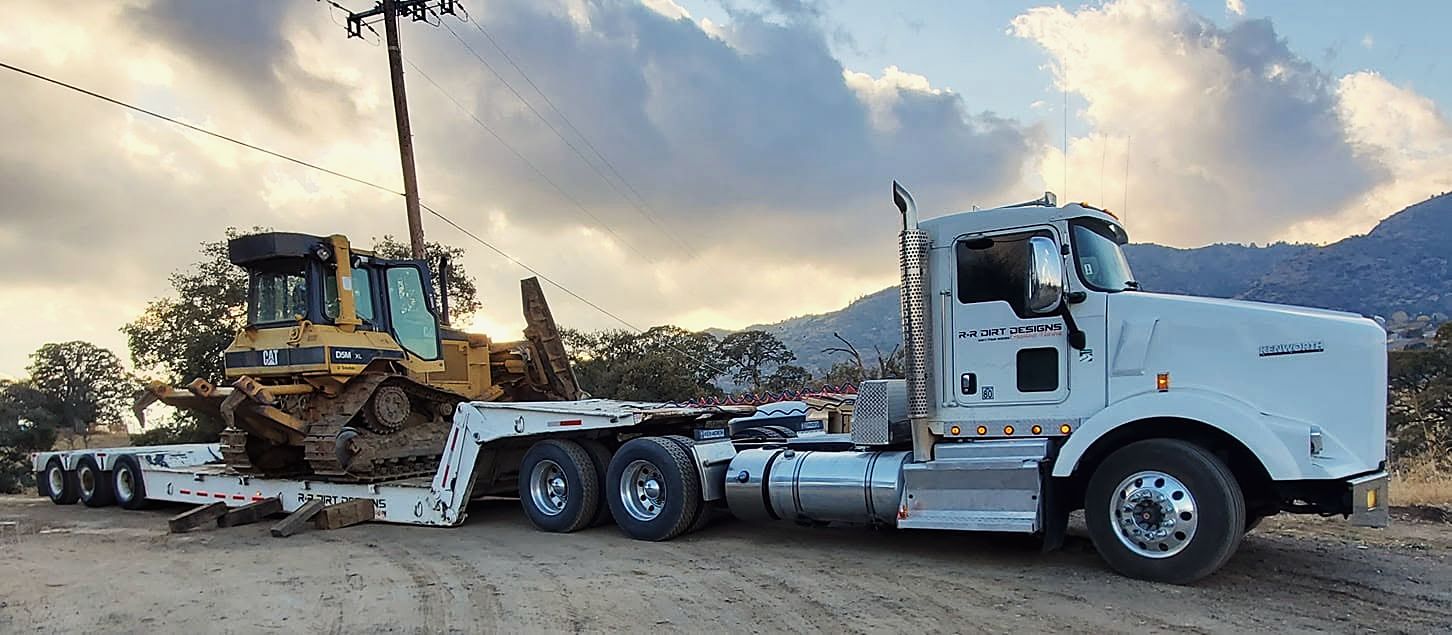 White semi truck hauling a track dozer on a lowboy trailer at sunset