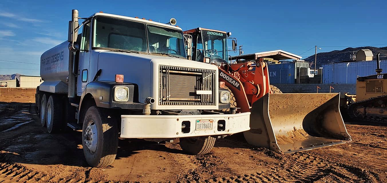 Water truck parked in front of a wheel loader on a dirt site